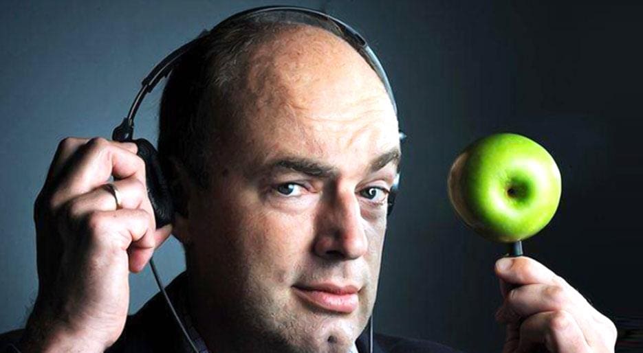 Professor Charles Spence with headphones plugged into an apple looking at the camera 