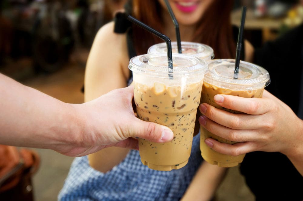 Three people holding iced coffees together