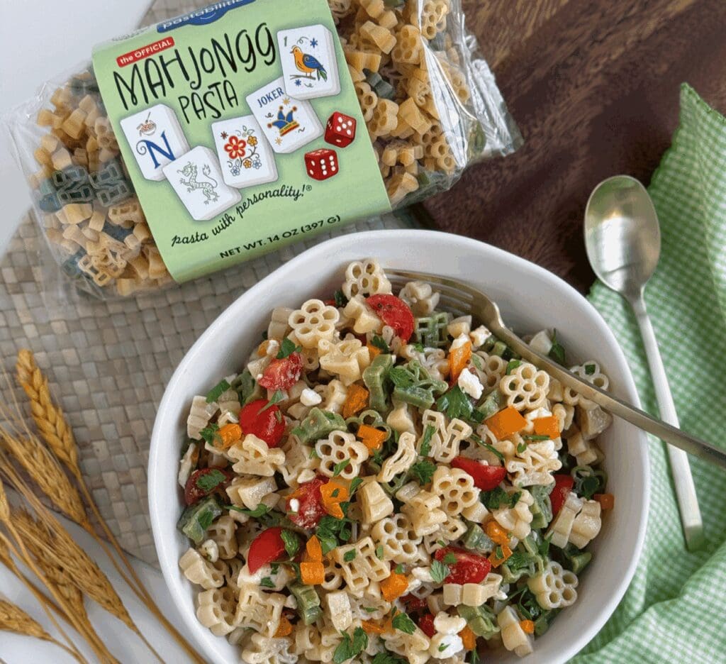 Mahjongg shaped pasta in a packet next to a pasta salad made with the same pasta 
