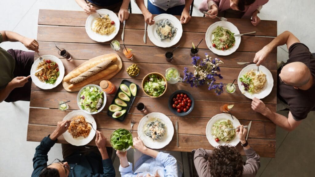 Picture of people eating together around the table. Credit to Canva.