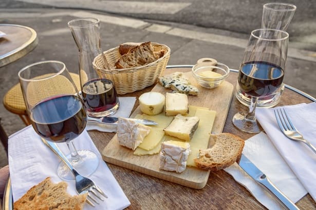 A cheese board with many different cheese and glasses of red wine 