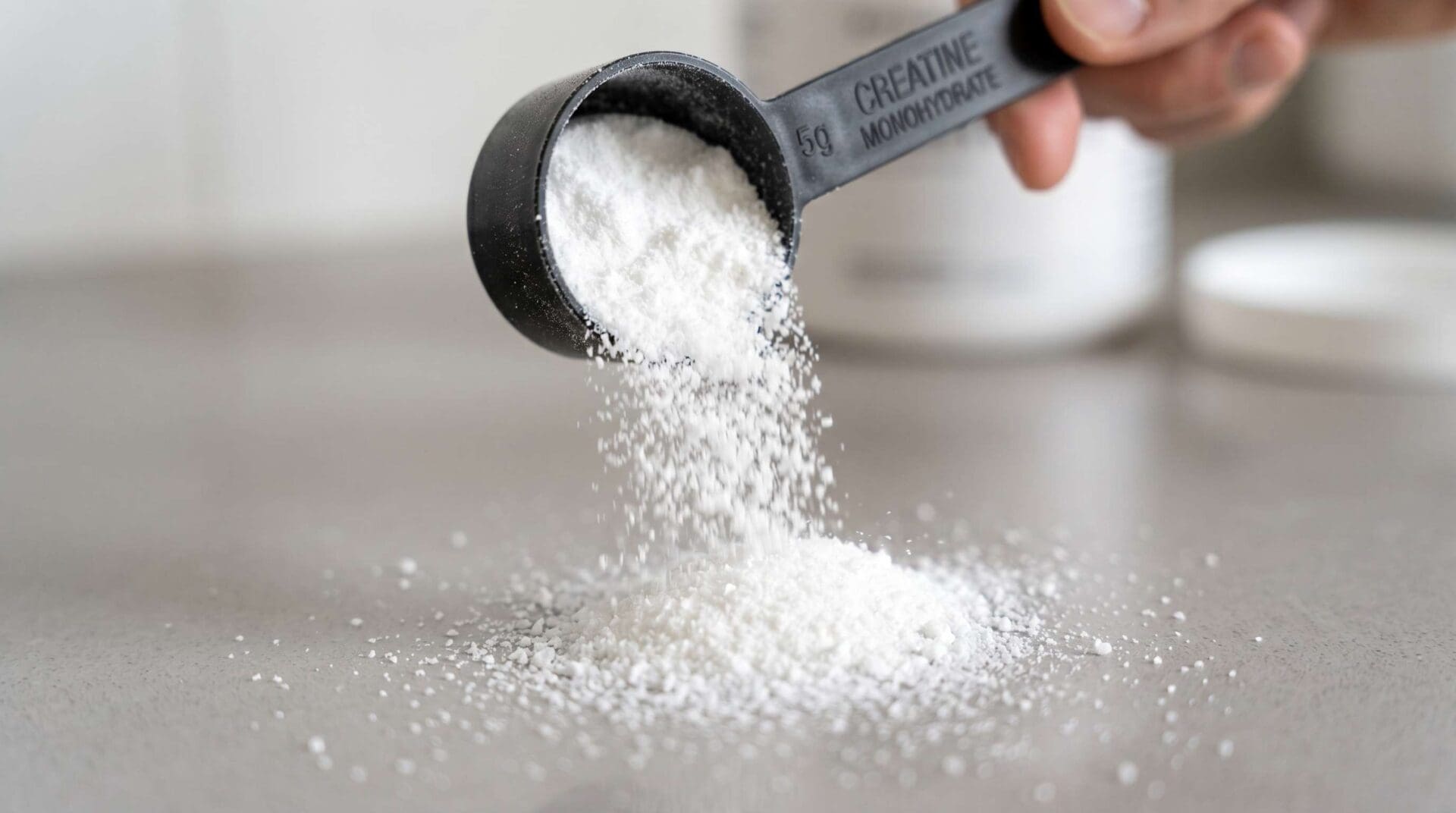 Creatine Monohydrate A scoop of creatine monohydrate pouring onto a grey surface