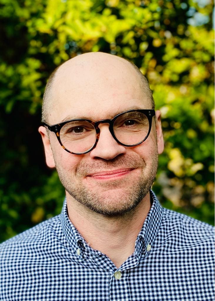Dr Neil Buttery, Food Historian, smiling in front of a natural green backdrop