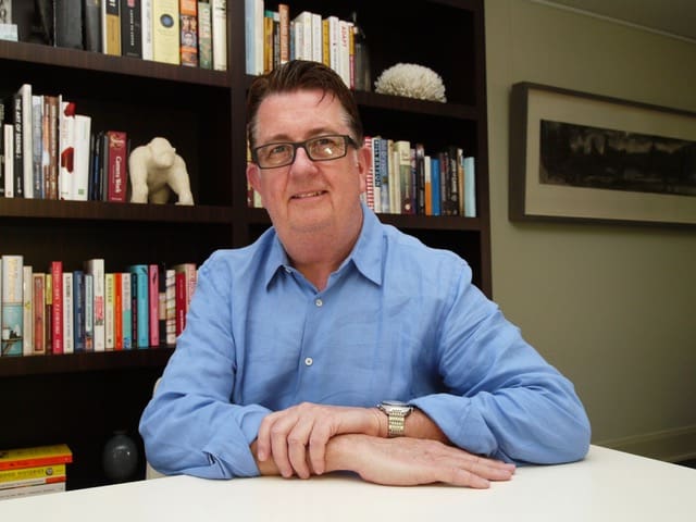 Picture of Dr. John Prescott sitting in front of his desk, with book filled shelves behind him.