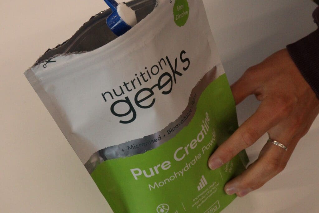 Hand holding a pouch of creatine with a scoopful coming out the top.