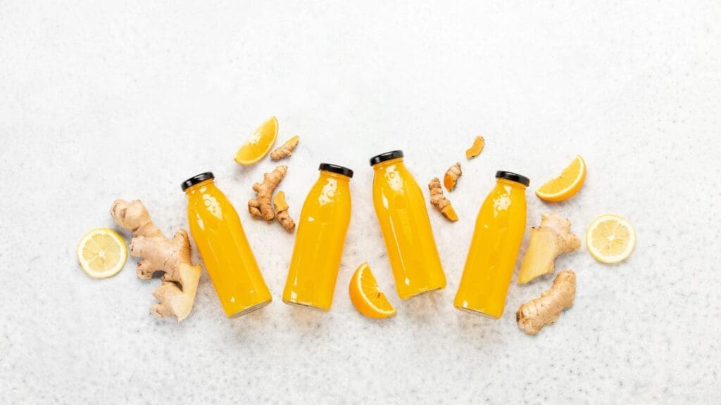 Picture of four bottled ginger, lemon and orange juice, with pieces of oranges, lemon slices, and gingers around them.