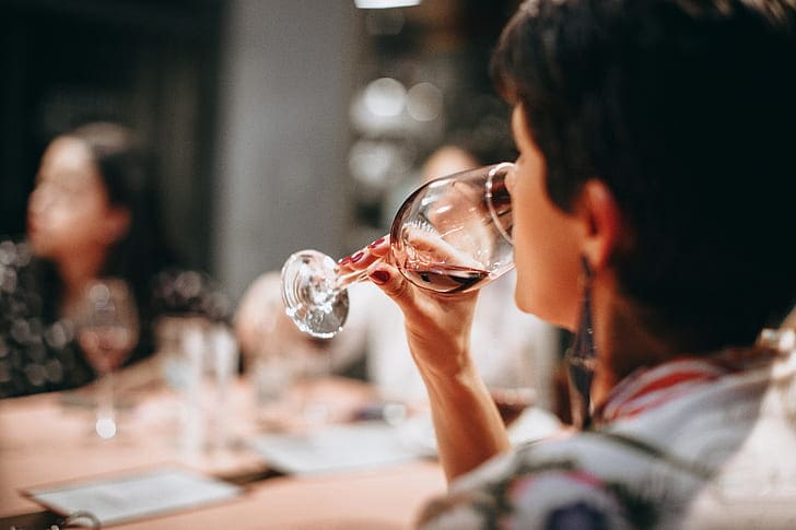 A person drinking from a glass of red wine
